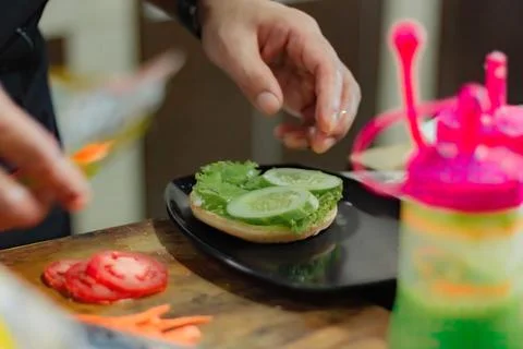 Chef puts tomato slice for burger filling, on kitchen utensils background. Stock Photos
