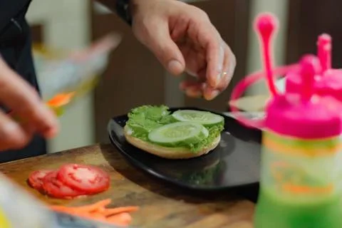 Chef puts tomato slice for burger filling, on kitchen utensils background. Stock Photos