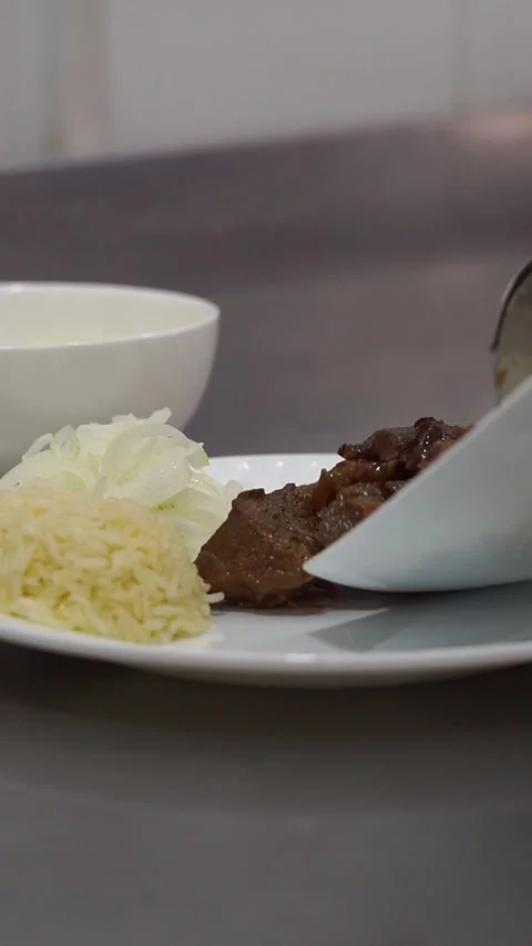 Chef putting delicious roasted meat next to rice and sliced onions on a white pl Stock Footage 342345280