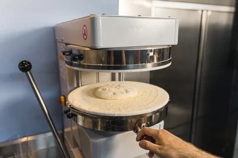 Chef putting the dough in the machine to press and make pizza Stock Photos