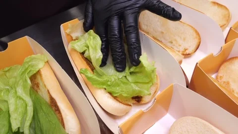 Chef putting fresh lettuce on toasted buns in a commercial kitchen assembly line Stock Footage 324710976