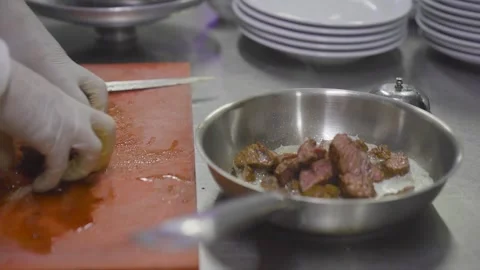 Chef putting sliced grilled meat into stainless steel pan in restaurant kitchen Stock Footage 332116359