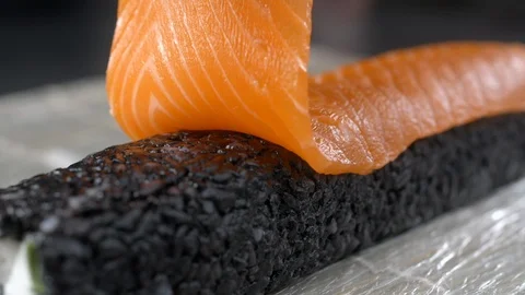 Chef raw salmon to the black rice roll and makes sushi, cooking the raw red fish Stock Footage 116504464