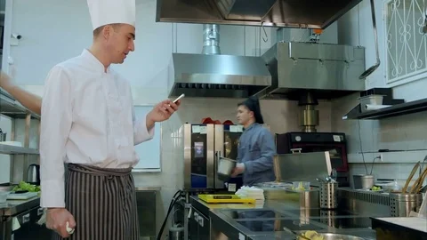 Chef reading something from his phone and talking to one of the cook trainees Vidéo 72324194