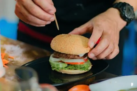 Chef ready to serve burger, on kitchen utensils background Stock Photos