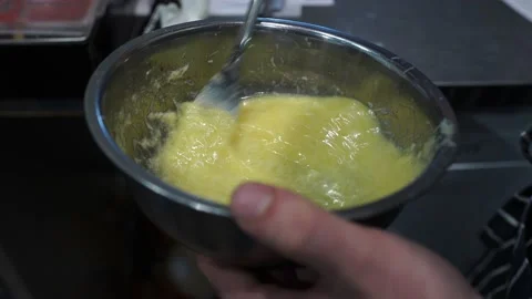 A chef in a restaurant kitchen in an apron shakes eggs in a bowl with a fork Stock Footage 141244248