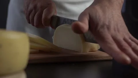 Chef in restaurant kitchen beautifully cuts the hard cheese with a large knife. Vidéo 143487095