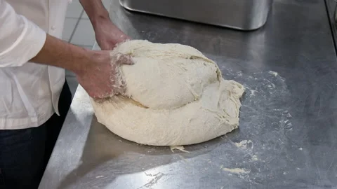 Chef at a restaurant kitchen bench folding a large dough to make bread Video stock 221331473