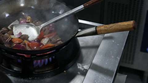 Chef in a restaurant kitchen cooking meat with vegetables in a wok Stock Footage 220777107