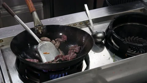 Chef in a restaurant kitchen cooking meat in a wok Stock Footage 221043476