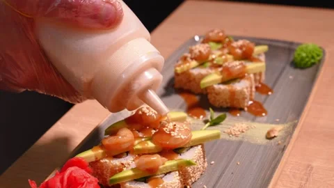 Chef in restaurant kitchen decorating delicious rolls with sesame sauce bottle Vidéo 269546555