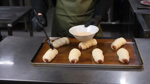 Chef in restaurant kitchen preparing sausage buns brushing dough with egg white  Stock Footage 333784332