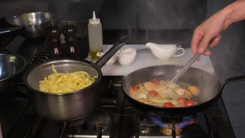 Chef in restaurant kitchen preparing seafood pasta frying seafood on hot skillet Stock Footage 334126562