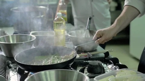 Chef in restaurant kitchen at stove with pan, doing flambe on food Stock Footage 76140957