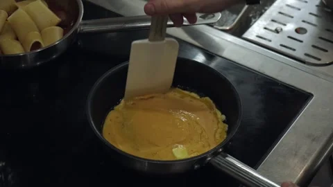 Chef of restaurant mixing eggs on hot pan on electric stove in kitchen Stock Footage 240653629