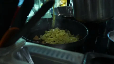 Chef in a restaurant puts boiled pasta with steam on a frying pan with tweezers Stock Footage 141242925