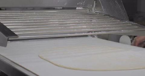 Chef rolling the dough on a rolling machine. Fresh dough coming out of a dough Stock Footage 287479592