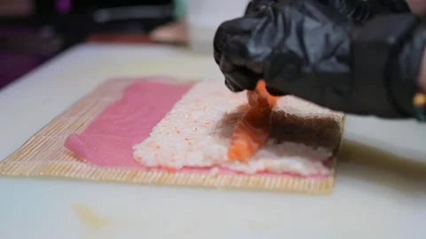 Chef rolling sushi with a bamboo mat, gloved hands guiding the nori sheet filled Video stock 293501904