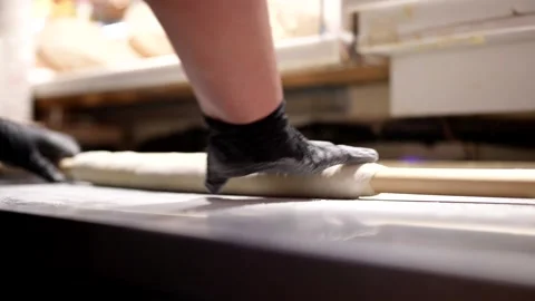 A chef rolls dough with a rolling pin on a floured metal surface, wearing black  Stock Footage 313883808