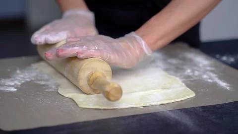 A chef rolls out puff pastry in flour with a wooden rolling pin on baking paper Stock Footage 260736712