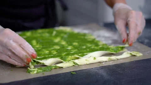A chef rolls ribbons of puff pastry with green vegetable paste. Making grissini Stockbeeldmateriaal 260736756