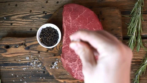 Chef Salt a Raw Fresh Steak with Pepper and Rosemary on Wooden Cutting Board Stock Footage 120569778