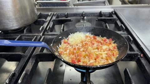 Chef sautéing chopped vegetables in a pan over a gas stove 스톡 동영상 344100127