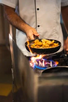 Chef sautes bite sized pieces over gas flame at Maldives resort kitchen Stock Photos