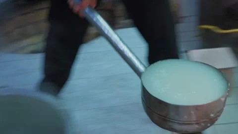 Chef scoops cooked rice from large ancient cauldron with long-handled ladle Видео 346700086
