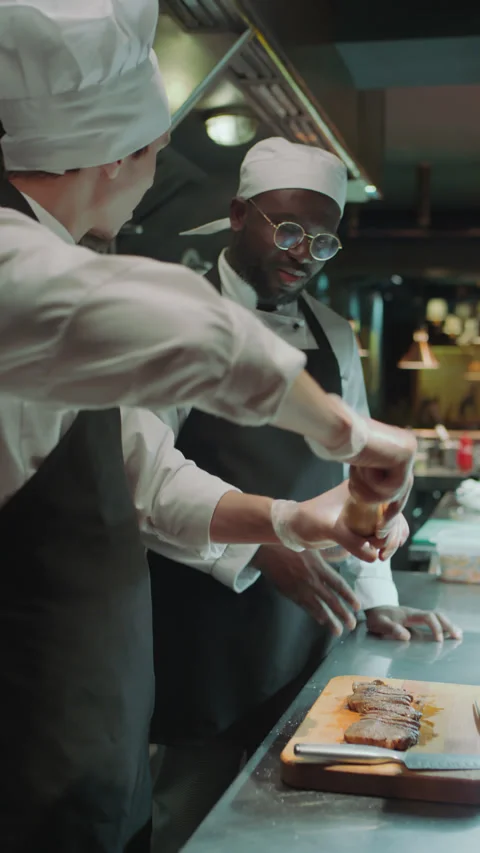 Chef Seasoning Meat Steaks as Apprentice Watching His Work in Kitchen Stock Footage 273452322