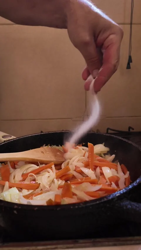 Chef seasoning sliced carrots and onions in a frying pan Stock Footage 329054476