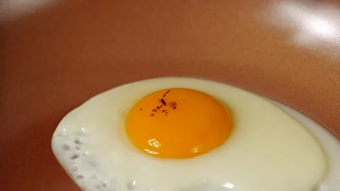Chef seasons a frying egg with ground pepper in a frying pan, slow motion Vídeo Stock 113595082