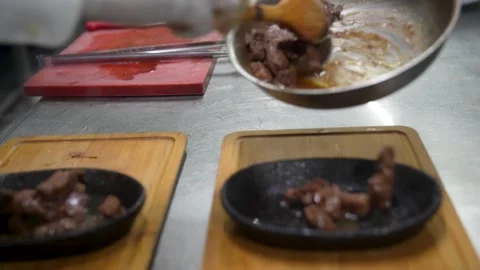 Chef serving cooked beef steak from pan to cast iron plates in kitchen Video stock 332116402
