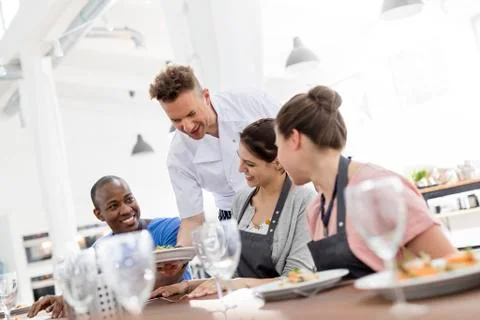 Chef serving cooking class students at table Stock Photos