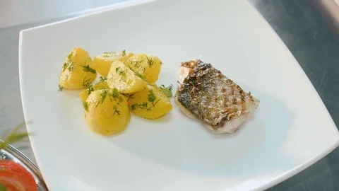 Chef serving a dish of prepared potatoes with herbs and fish in white plate. Stock Footage 91735175