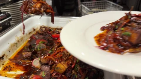 A chef serving roasted meat with vegetable garnish from a buffet warmer onto a 库存影片 345745763
