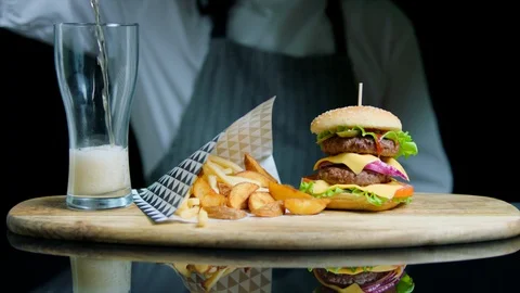 Chef serving set of tasty burger, french fries, pouring beer into glass on Stock Footage 92497073
