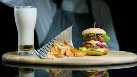 Chef serving set of tasty burger, french fries, pouring beer into glass on Stock Footage 92499249