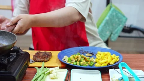 Chef serving steaming sautéed vegetables onto plate during steak dinner Stock Footage 345379671