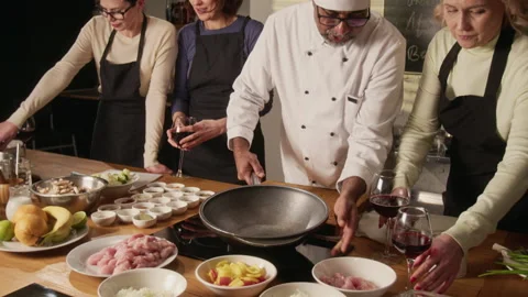 Chef Setting Up Pan on Stove During Cooking Master Class with Group of Women Stock Footage 332575147