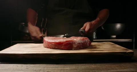 Chef sharpening his knife in front of raw piece of steak. Cooker preparing his 库存影片 144564021