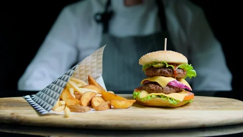 Chef is showing thumb out of focus and set of tasty burger, french fries, beer Stock Footage 92495483