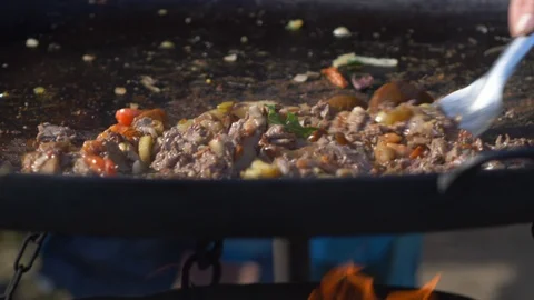 Chef shuffles meat from griddle with fire burning underneath Stock Footage 108564427