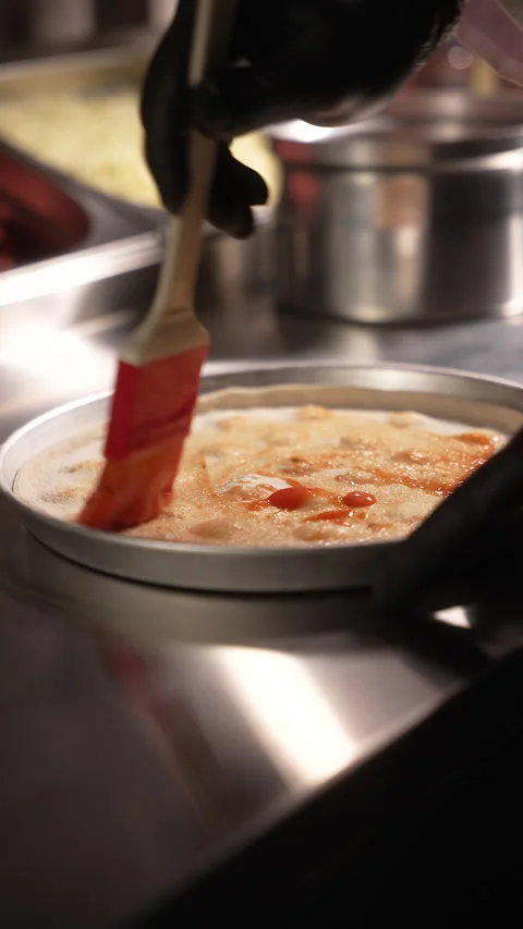 A chef skillfully brushes sauce onto a freshly made pizza base Stock Footage 315305313