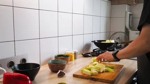A chef skillfully chops fresh vegetables on a wooden cutting board in a bright 動画素材 316481544