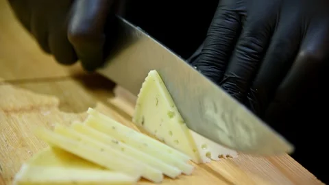 Chef slices cheese into thin pieces on wooden cutting board with knife Stock Footage 336677900