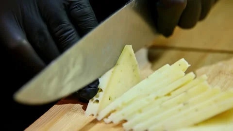 Chef slices cheese into thin pieces with knife on wooden cutting board Stock Footage 337229497