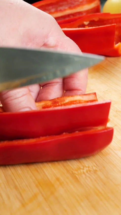 	A chef slices fresh red bell pepper into thin strips on a wooden cutting board. 库存影片 341684287
