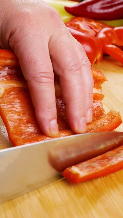 Chef slices fresh red bell pepper into strips on a wooden cutting board.  Video stock 341684298