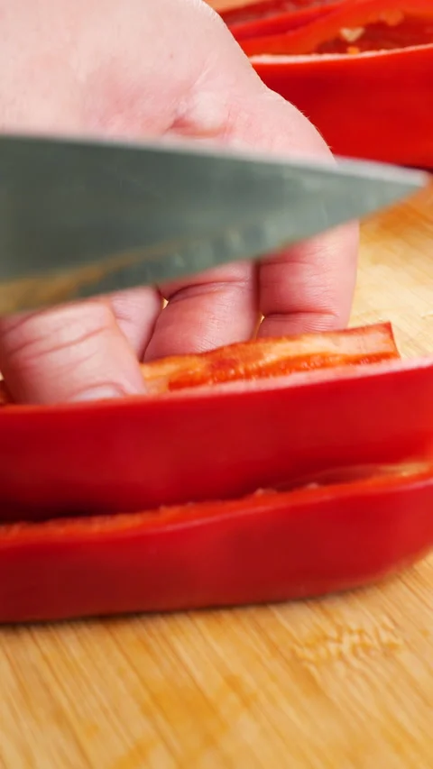 A chef slices fresh red bell pepper into thin strips on a wooden cutting board. Video stock 342284560